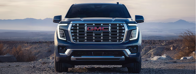Front view of a blue GMC Yukon Denali with its chrome grille, mountains behind