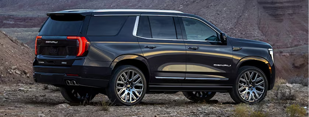 Black GMC Yukon Denali Ultimate parked on rocky ground, seen from the rear three-quarter angle