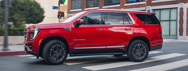 Red GMC Yukon Elevation driving through a city intersection, seen from the side