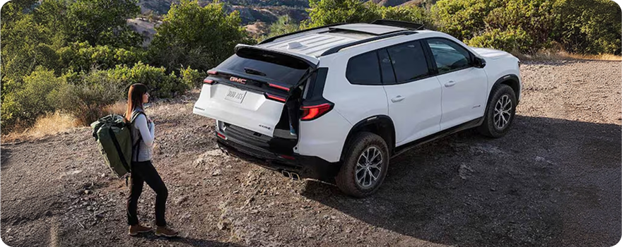 Hiker with a backpack walking up to a white GMC SUV as its power liftgate opens