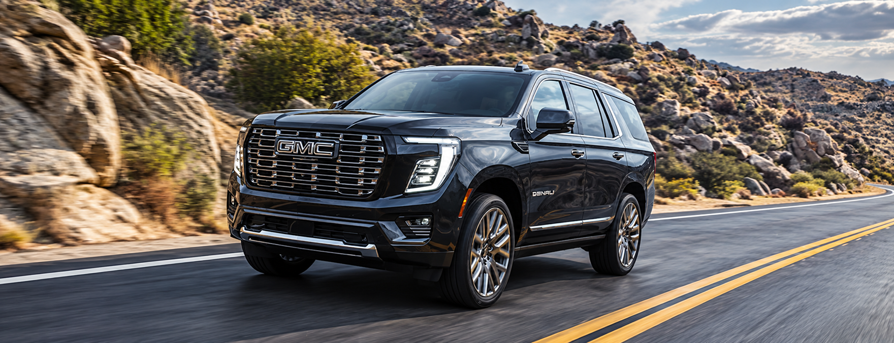Black GMC Yukon Denali rounding a curve on a rocky hillside road