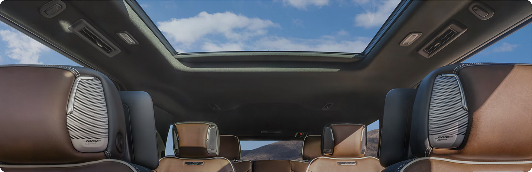 GMC Yukon Denali Ultimate cabin with brown leather seats and Bose headrest speakers under a panoramic sunroof
