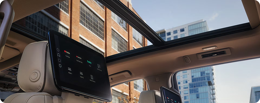 Panoramic sunroof above the rear-seat media screens in a GMC Yukon, city buildings overhead