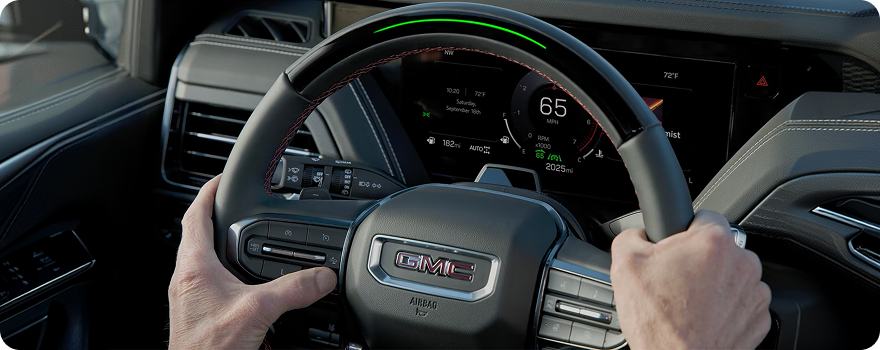 Hands resting on a GMC Yukon steering wheel with the Super Cruise light bar glowing green
