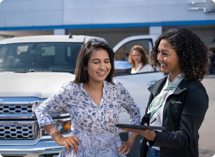 A salesperson showing a tablet to a smiling customer beside a white pickup on the lot