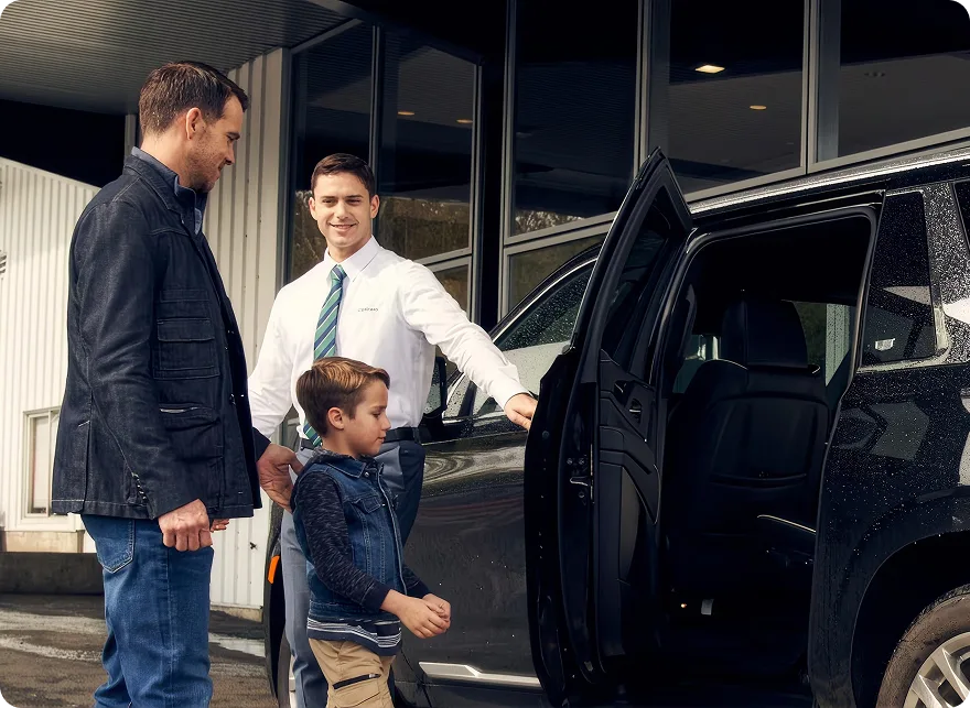 A salesperson opening the door of a black SUV for a father and his son