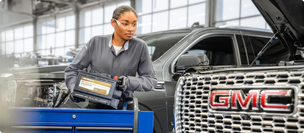 A technician testing a vehicle battery with a diagnostic tool under the hood