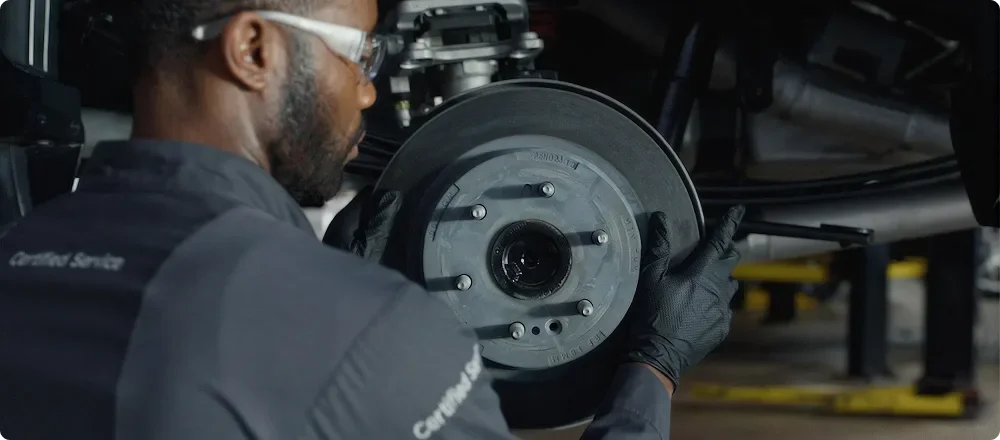 A technician inspecting a brake rotor and caliper on a raised vehicle